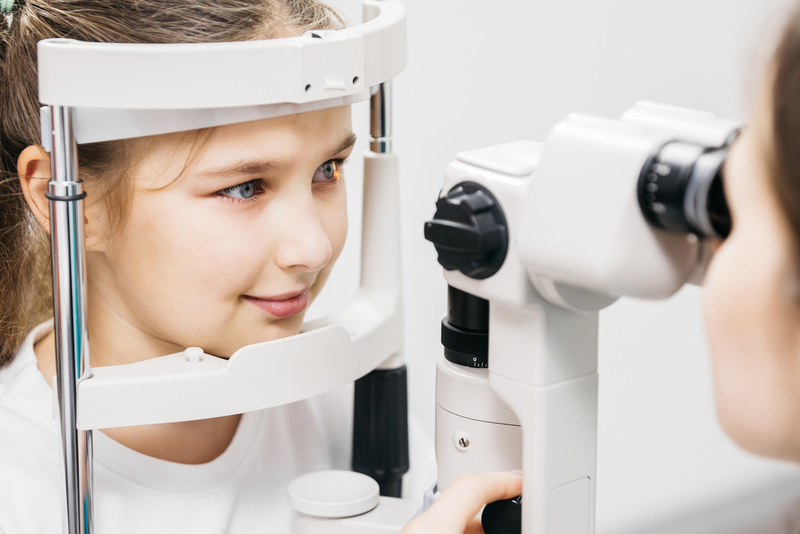 A child rests their chin on an eye exam machine while an eye care professional performs a vision test in a clinic.