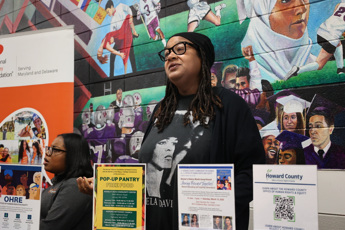 A woman with locs and black glasses speaks to a community member