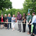 Howard County leadership cutting a green ribbon. County Executive Calvin Ball and Office on Aging Administrator Ofelia Ott hold the giant pair of scissors.