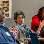 Korean woman with short greying hair speaking during a listening session, using her hands to gesture with palms open.