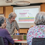 Three older women talking in front of a presentation slide on Transit 101.