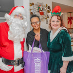 "Santa Claus", an older Black woman holding a Project Holiday care package, and "Santa's Elf" posing and smiling together.