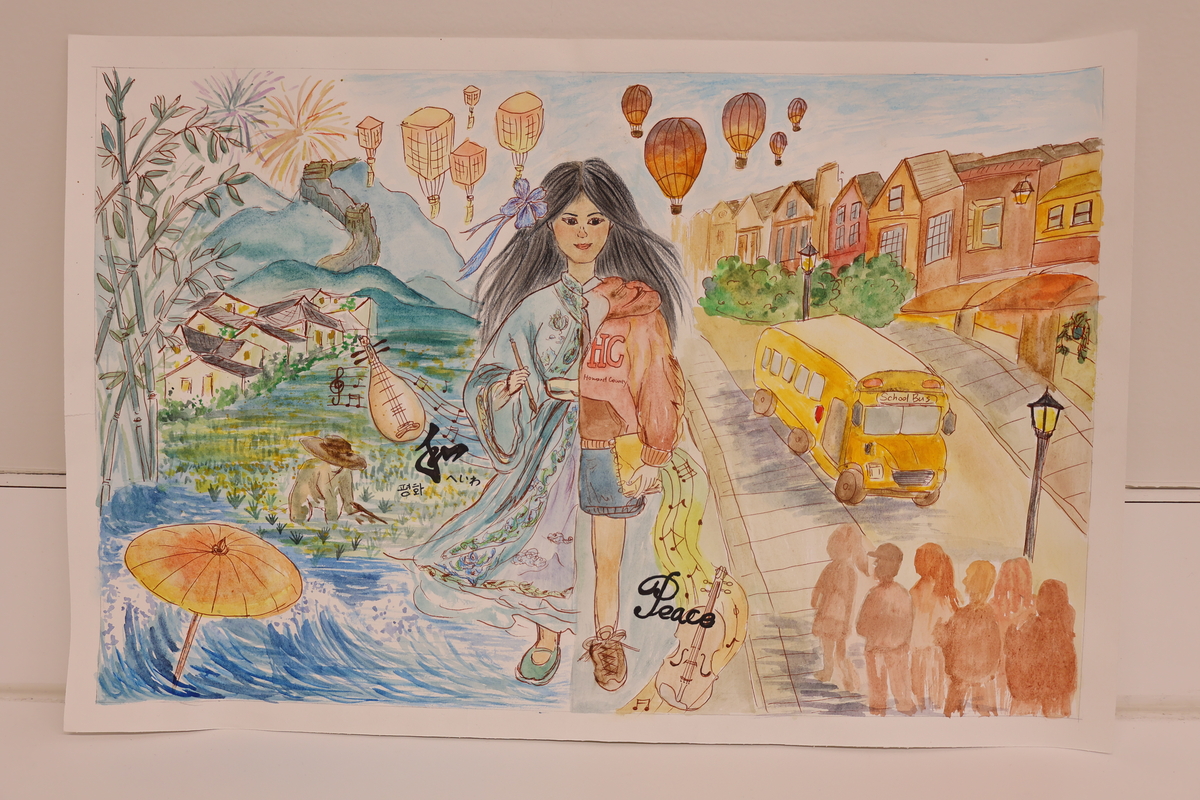 This artwork shows a girl walking the street. On one side are homes and children waiting for a school bus. On the other side are mountains and a man harvesting by the water.