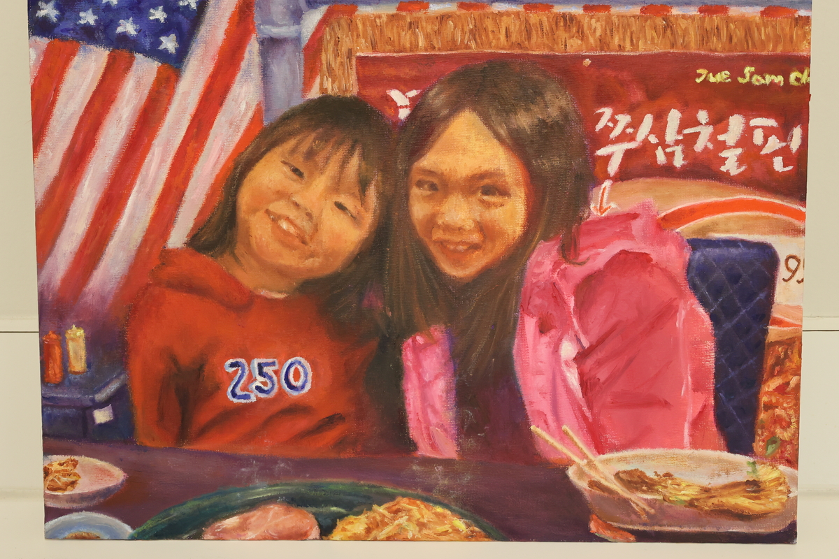 This artwork is of two children smiling sitting at a restaurant table with food in front of them.