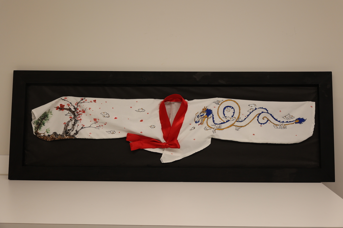 A small Asian style wrap jacket, with a red collar and image of a dragon on one sleeve, and cherry blossoms on the other sleeve.