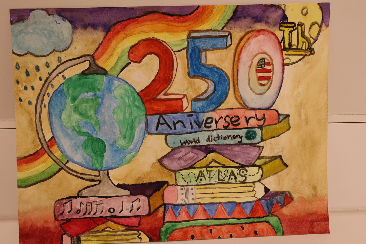 Child's drawing is of a rainbow, over a desk with books and a globe.