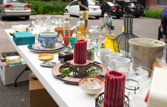 Table at yard sale with a variety of items including candles and mugs.