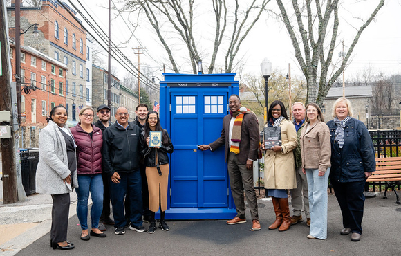 A photo of County Executive Calvin Ball and County staff and local Old Ellicott City community members standing in front of the County's new mobile Little Free Library the #HoCoTARDIS.