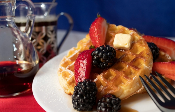 Waffles on a plate with strawberries and blackberries and syrup and butter.
