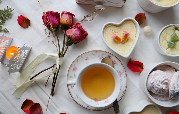 Dried roses, cup of tea and desserts on a table.