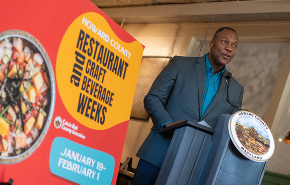 A photo of County Executive Calvin Ball speaking at the podium during the press conference announcing the launch of the 2026 winter season's Howard County Restaurant & Craft Beverage Weeks.