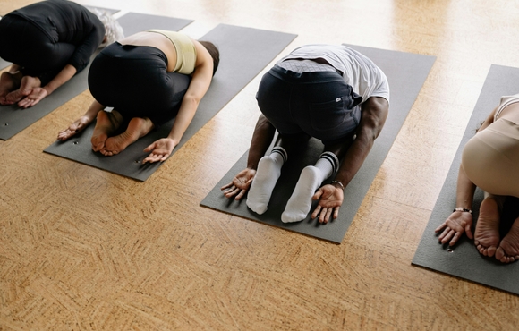 Four people facing down on yoga mats in child's pose.