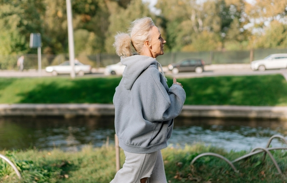Caucasian women with light colored hair in pony tail running in a grey sweatshirt outside.