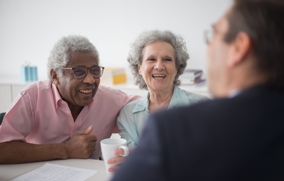 Black older adult male with Caucasian older adult female meeting with man at table.
