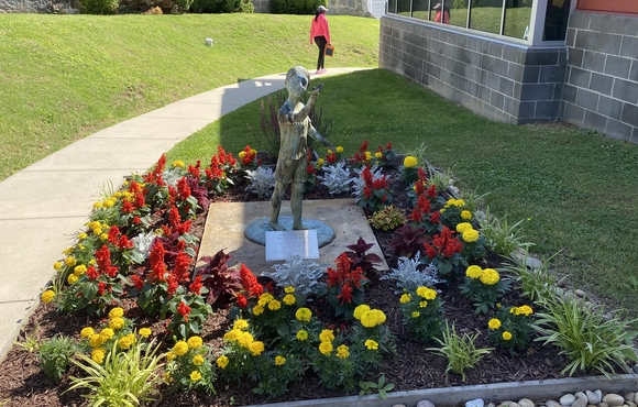 Linwood Center Garden. Statue of a child in a bed of red and yellow flowers