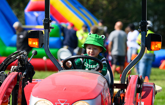 Child in a frog costume sitting on and playing with a red tractor