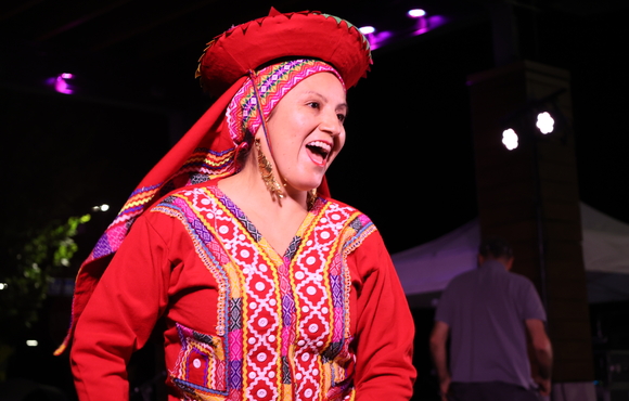 A woman in traditional Peruvian dress smiles while dancing on an outdoor stage. 