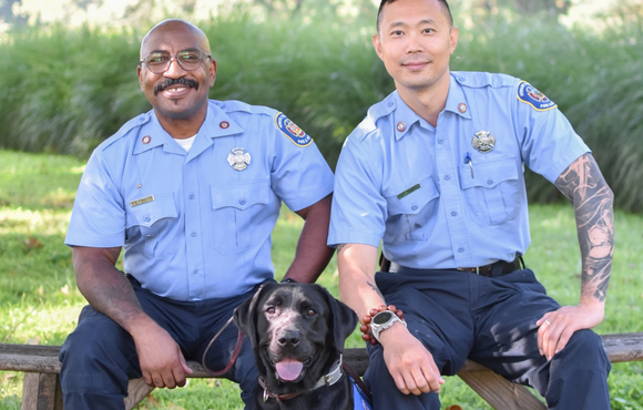 Two firefighter handlers sit with peer support dog