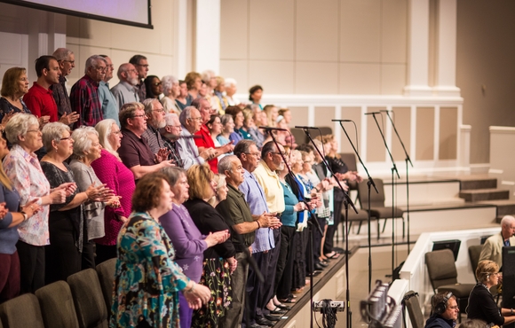 older adults singing on a tiered stage in front of an orchestra pit