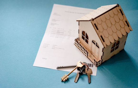teal background with a sheet of paper, keys, and a small model home with the latter two items being on top of the paper