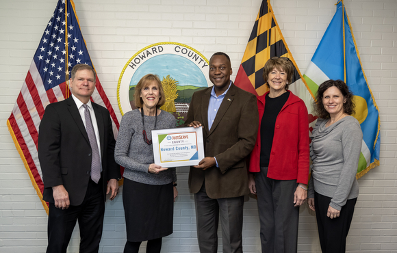 Calvin Ball pose with a group of people holding a certificate that recognizes Howard County as a JustServ county.