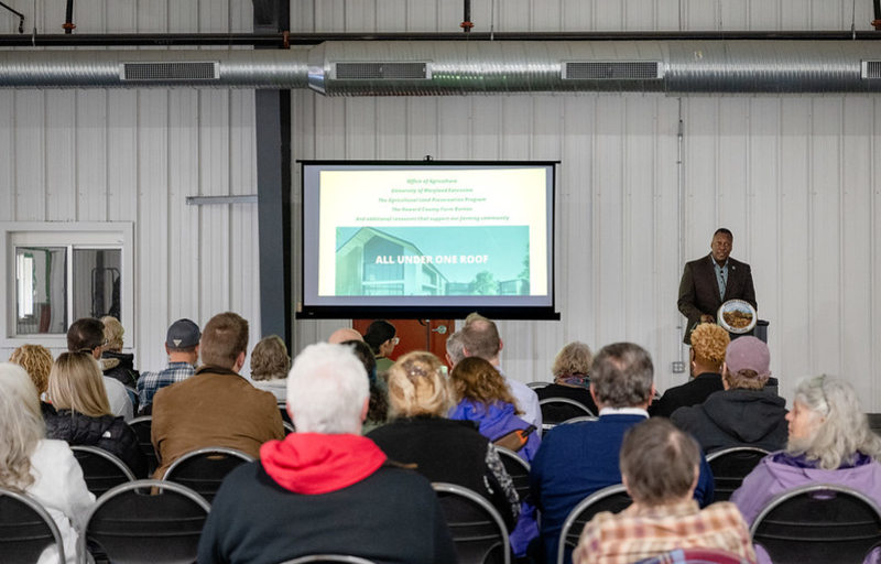 Howard County Executive Calvin Ball standing at a podium inside a Howard County Fairgrounds building delivering his State of Agriculture address to the county's farming community.