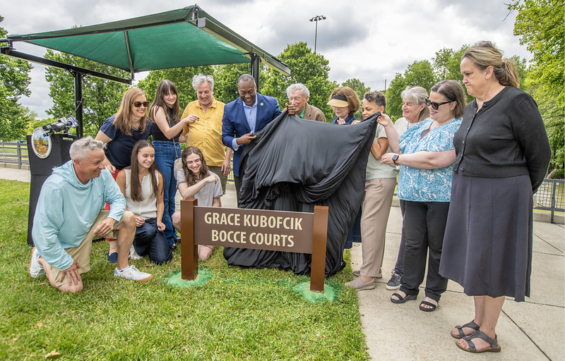 County Executive Calvin Ball and others pulling off the cover to unveil the new Grace Kubofcik Bocce Courts sign at Cedar Lane Park West.