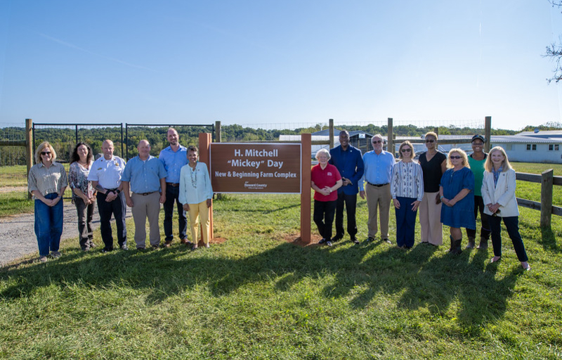 County Executive Calvin Ball, family members, friends, and community members posed by the new H. Mitchell Mickey Day New & Beginning Farm Complex sign at West Friendship Park.