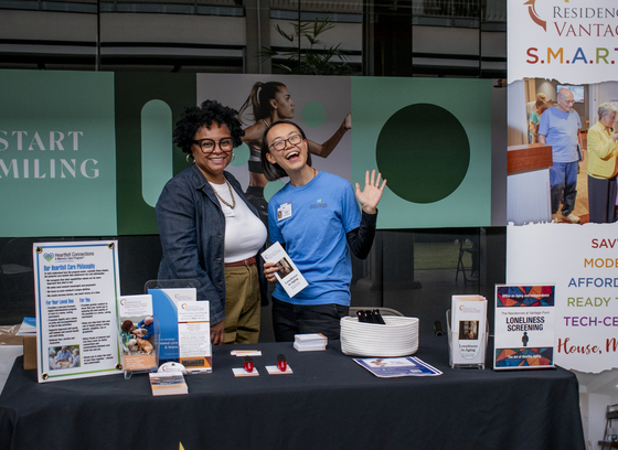 Two women smiling and posing together at a resource table at an event in the mall.
