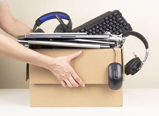 Caucasian person's arm holding cardboard box with laptops, keyboards and headphones.