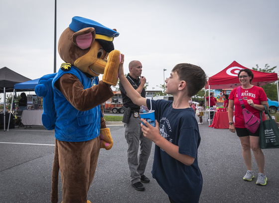 A person dressed as Chase from Paw Patrol high fives a child at National Night Out
