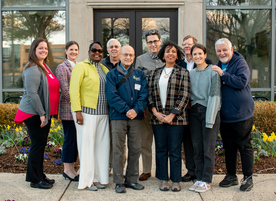 Group of commissioners standing in front of office building outside. Mix of women and men of various races and ages.