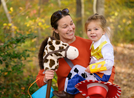 An adult and child pose outdoors. The child is wearing a costume.