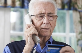 Older adult man on the phone holding a credit card.