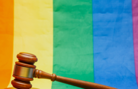 A wooden gavel resting on an LGBT Pride flag. 