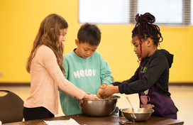 three children mixing baking ingredients in a single metal bowl