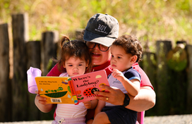 Two toddlers getting read a book by their mother. 