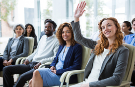 3 women and 1 man sitting in a classroom and women to the far right is raising her hand