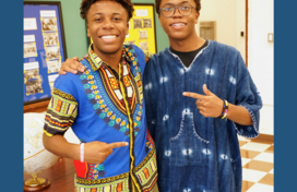Two young people in traditional African clothing smile at the camera. 