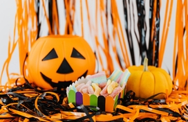 Pumpkin, plastic jack-o-lantern and cup of candy sitting atop black and orange streamers.