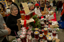 Craft items and jams on a table with vendors selling.