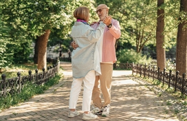 Older adult couple dancing on a sidewalk in a park on a nice day.