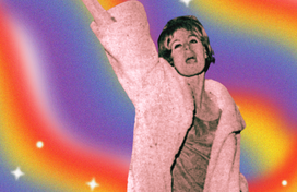 An image still of a trans woman in a pink faux fur coat with her fist extended over her head on a rainbow background. 