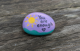 Rock painted with "You are enough". Also includes a sun and a heart.