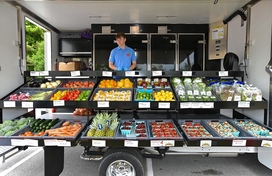 A man smiling standing outside in front of fruits and vegetables laid out in boxes