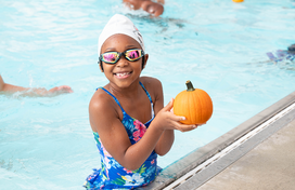 Smiling girl looking at camera holds pumpkin near edge of pool