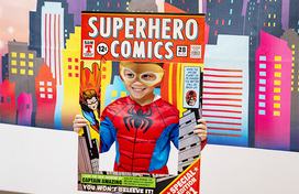 Kid in spiderman costume holding posing for a photo while holding a cardboard frame saying "Superhero Comics"