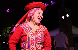 A woman in traditional Peruvian dress smiles while dancing on an outdoor stage. 