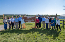 County Executive Calvin Ball, family members, friends, and community members posed by the new H. Mitchell Mickey Day New & Beginning Farm Complex sign at West Friendship Park.