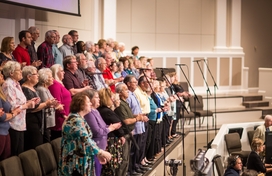 older adults singing on a tiered stage in front of an orchestra pit
